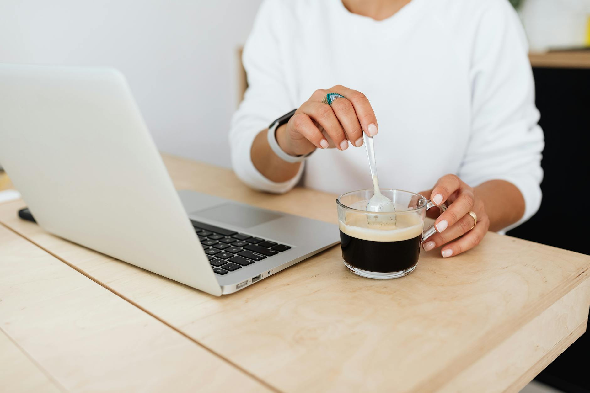 close up of woman sitting at the desk with a laptop and stirring her coffee