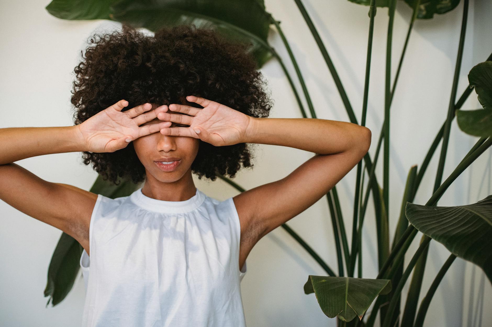 black woman covering face with hands standing near potted plant | article heal money shame