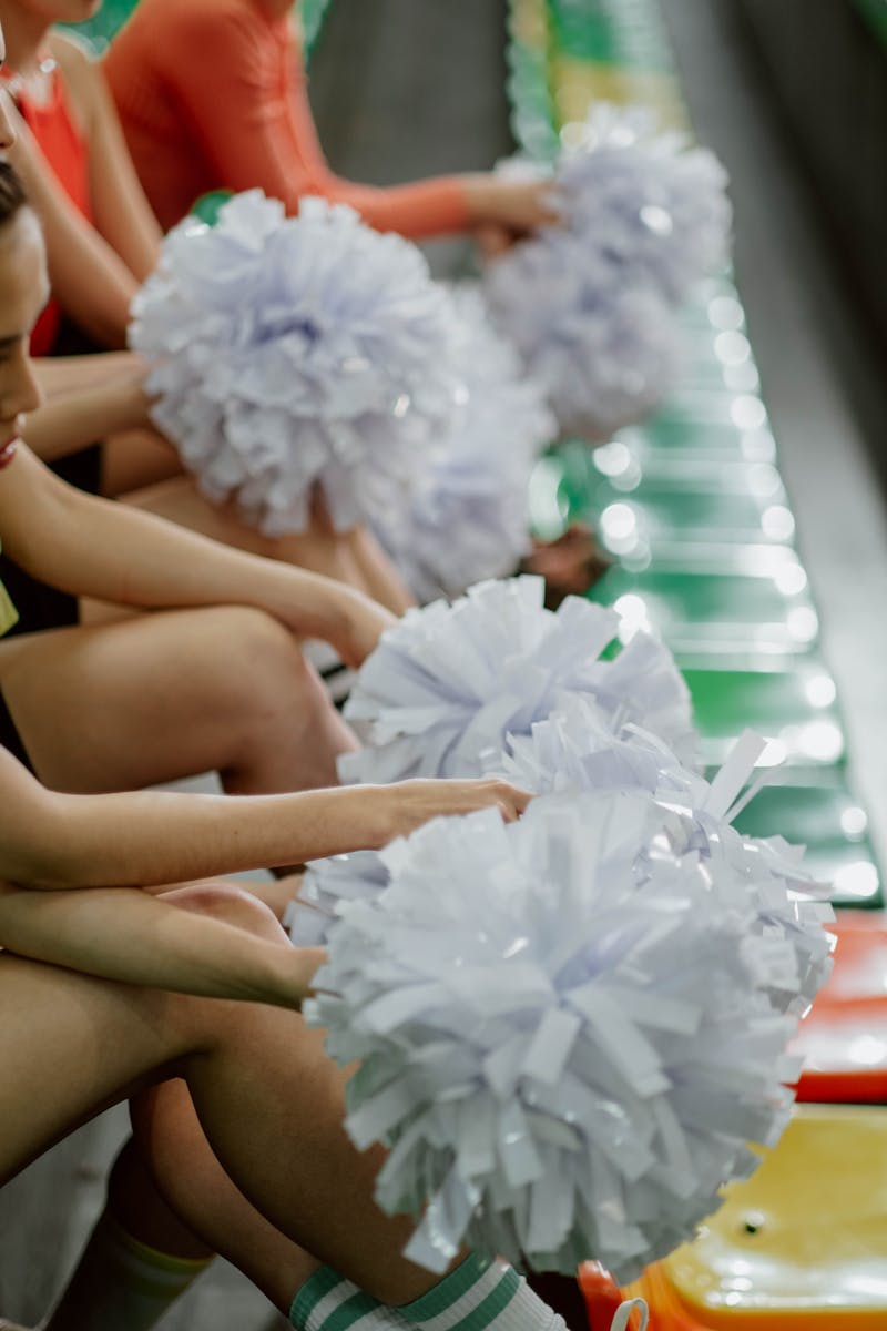 A group of cheerleaders holding pom poms while sitting on colorful stadium bleachers. be your cheerleader