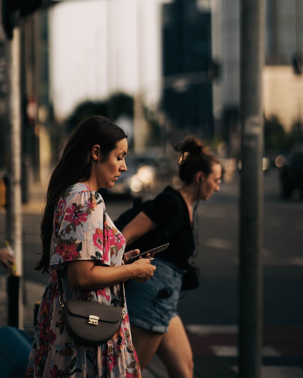 a woman in floral dress holding her phone on the street